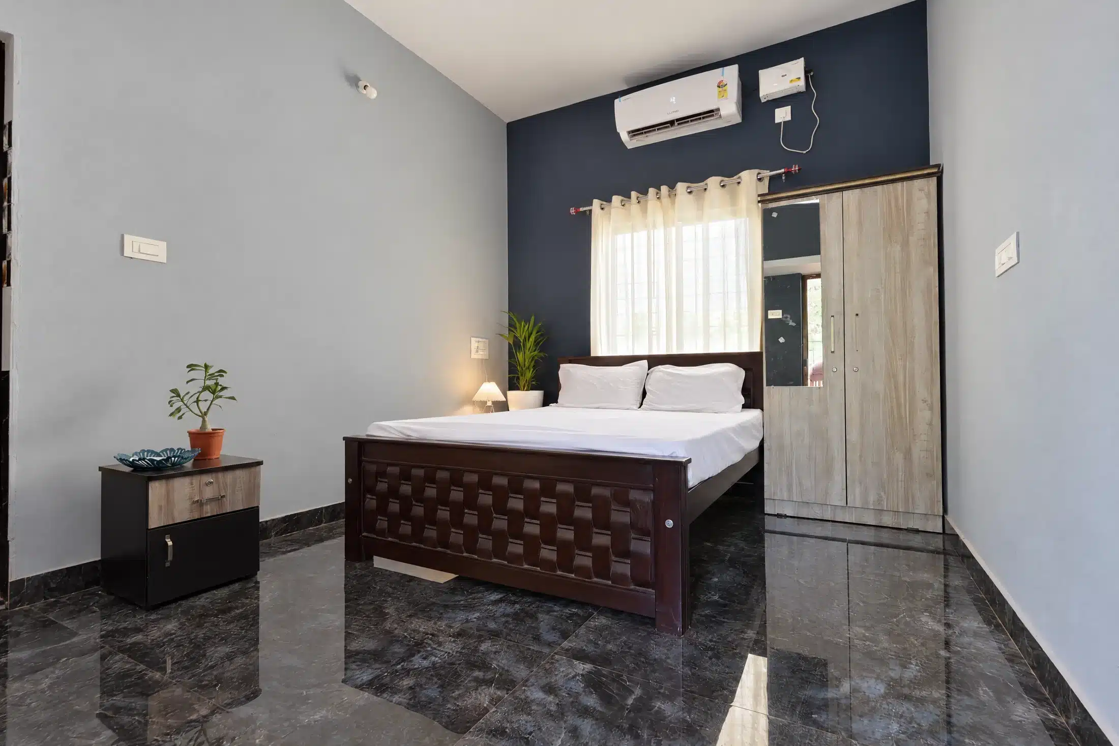 Standard couple room viewed from the window side with queen bed and bedside table